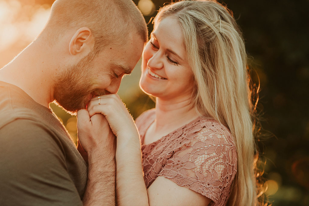 Ein glückliches verlobtes Paar während eines Paarshootings bei dem er ihre Hand küsst