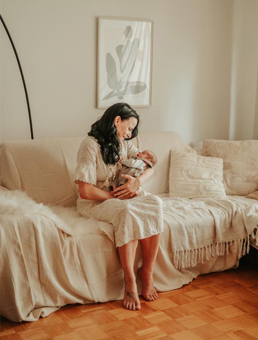 Frisch gebackene Mama hält ihr neugeborenes Baby liebevoll im Arm bei sich Zuhause